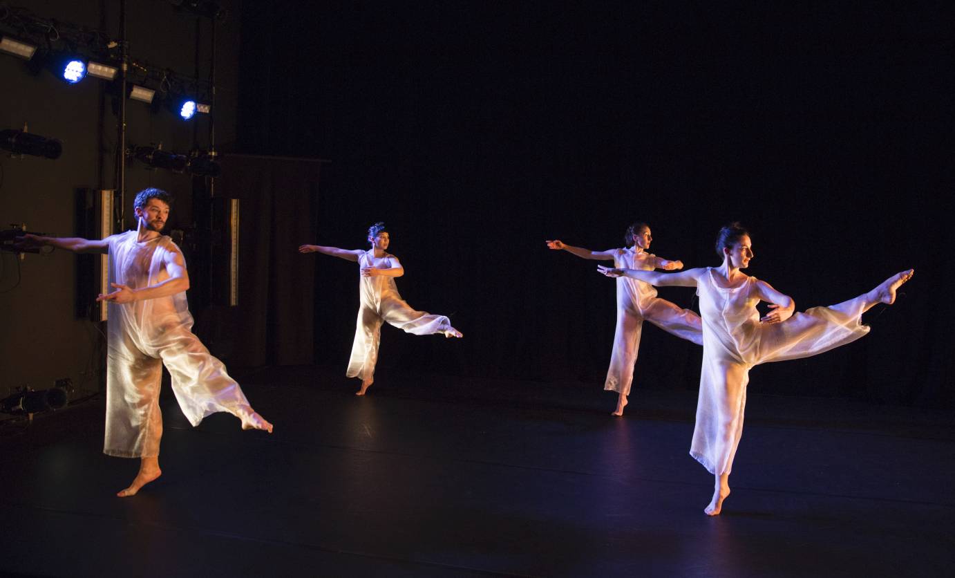 Four dancers extend their legs to the side, their arms in low third position
